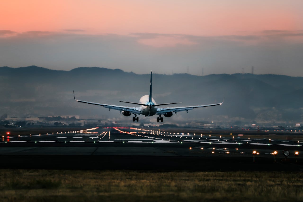 about-img-01 Dramatic view of a commercial airplane landing on a runway at sunset with mountains in the background.